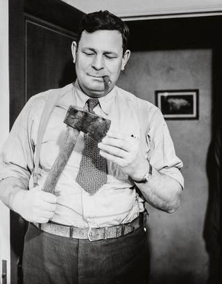 A cigar-chomping detective examines the murder weapon, c1940
