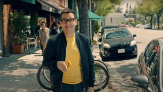 Paul Marcarelli smiles on a street in daylight while holding a yellow phone for Sprint.