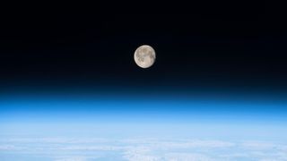 thin blue haze of earth's atmosphere with the moon shining above. 