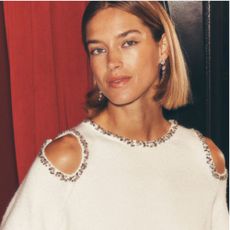 Blonde woman wearing cream sweater with jewelled neckline and shoulders, red curtain behind