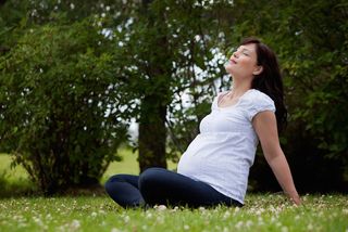 A pregnant woman sits outdoors, breathing deeply