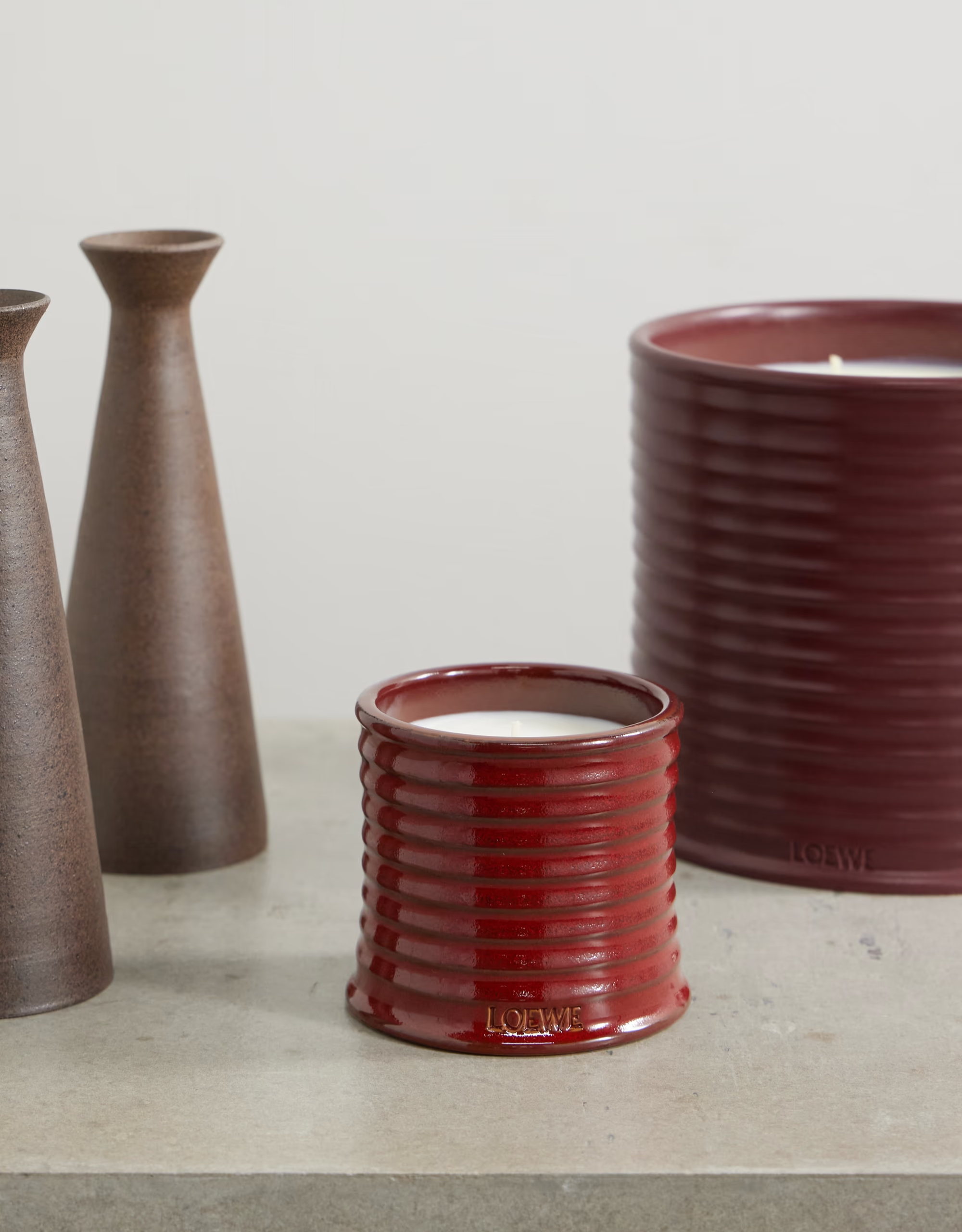 A pair of red glossy ceramic sweet almond candles from Loewe beside tall vases