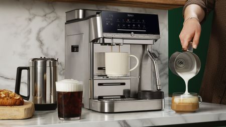 Ninja AutoBarista Pro coffee maker on kitchen counter, with person's hand pouring milk out of pitcher