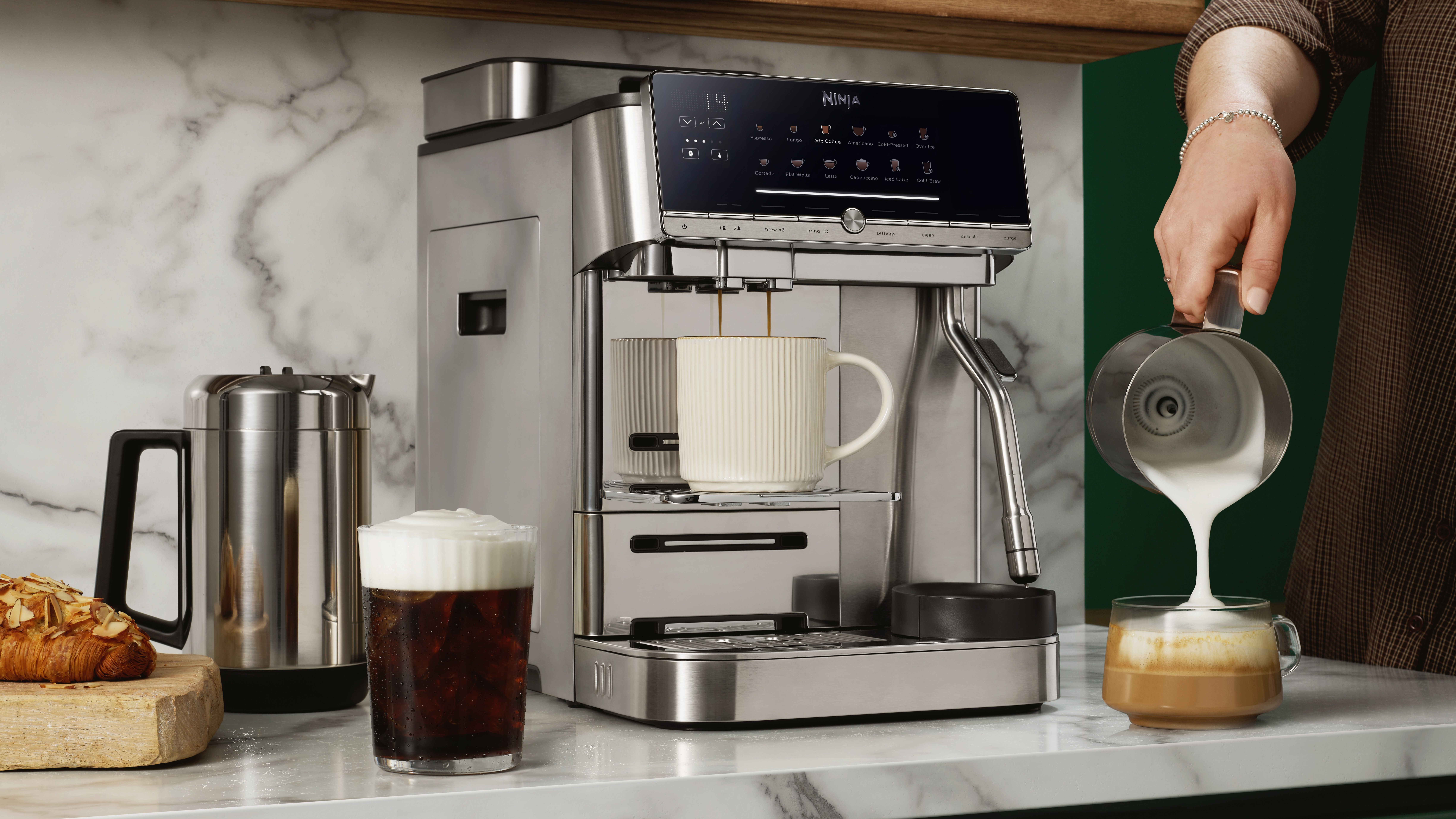Ninja AutoBarista Pro coffee maker on kitchen counter, with person's hand pouring milk out of pitcher