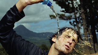 Young man pouring water on self from bottle, washing mud off face