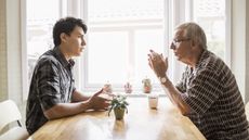 A grandfather and his grandson have a serious discussion across the dining room table.