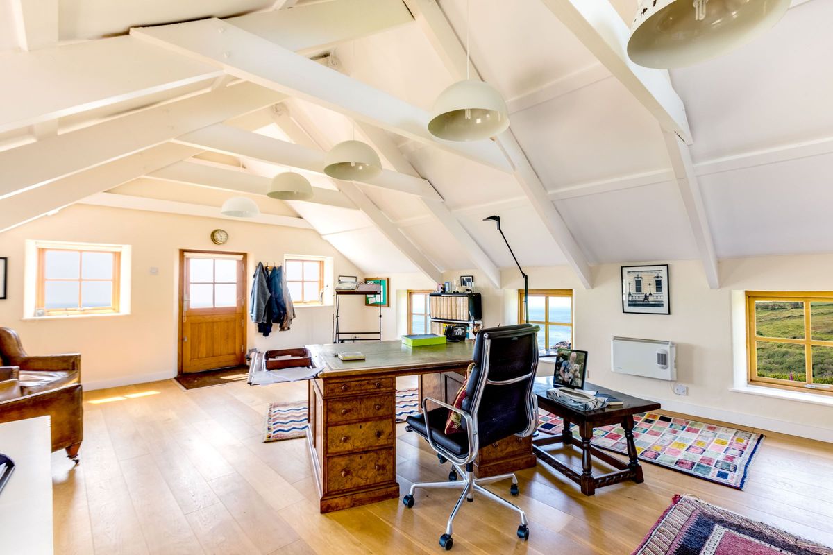A library with wooden flooring and white triangle ceiling beams has a wooden desk and chair and writing table in the corner