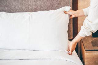 A person places a pillow on a bed
