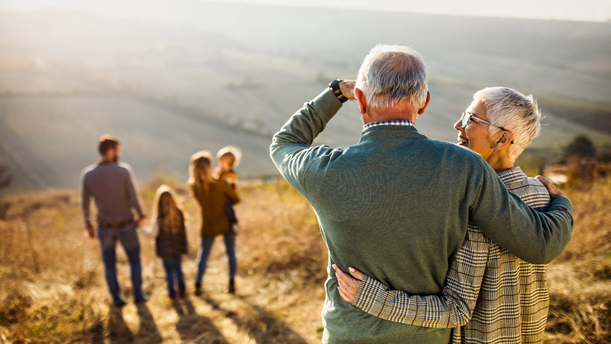 Rear view of senior couple looking at their family on a hill on a sunny autumn day