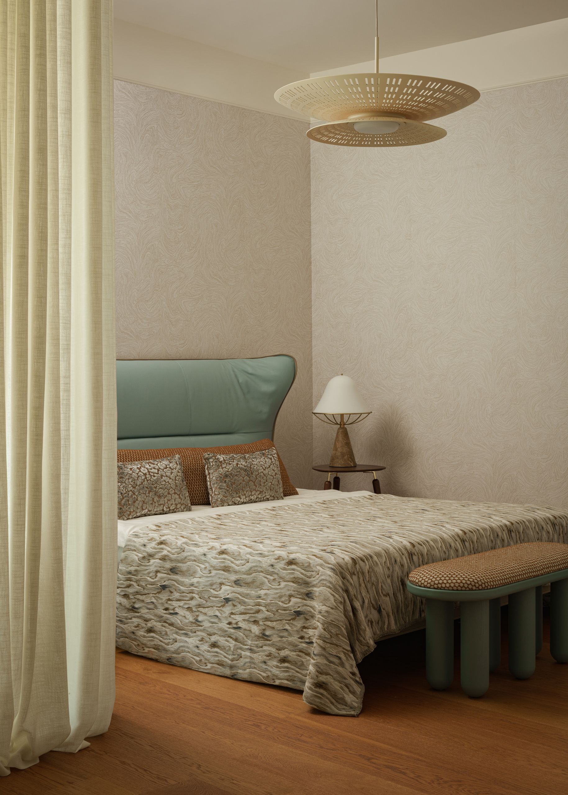 Image of a greige bedroom with a bed that has a large light blue headboard, gray marbled bedding, and orange detailing. There is a pendant light, a lamp, a bench seat and a curtain in the room.