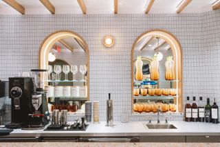 Cafe with a coffee maker and two arched spaces with shelves holding glasses and cups at Manifest Washington designed by Snarkitecture
