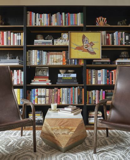 Bookshelves with books, accessories and artwork with two armchairs and side table in front and rug on floor