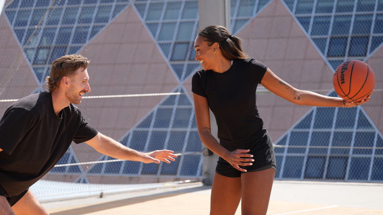 A man and a woman playing basketball. They're both smiling while the woman holds the ball.