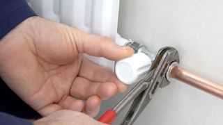 Close up of person fitting a radiator valve with pliers