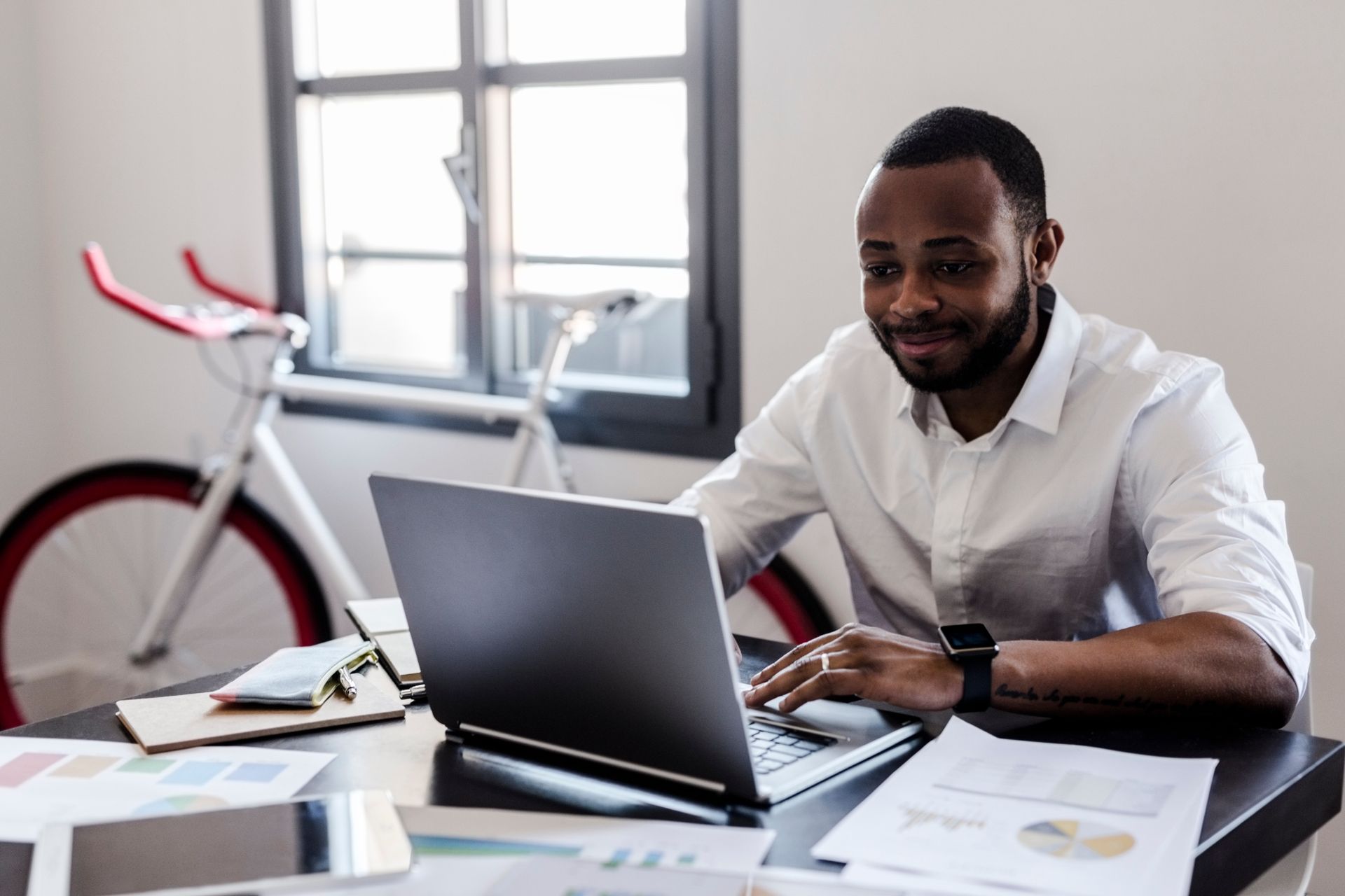 The importance of cycle insurance. Buying on line on a laptop computer on a desk with a white fixie bike with bullhorn handlebars and two brake levers behind, leaning against a window with four panes of glass