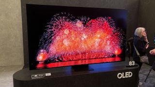 Samsung S95F OLED TV on a grey stand with fireworks on screen