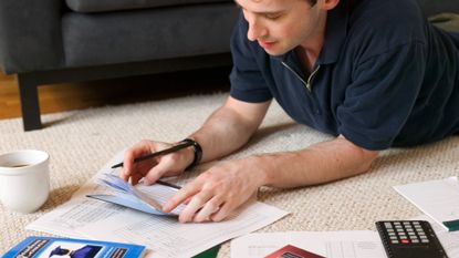 Male student laying on the floor sorting out his student loan bills with a calculator and checkbook 