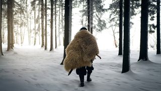 A modern depiction of an ice age warrior wearing an animal fur and walking in a snowy forest.
