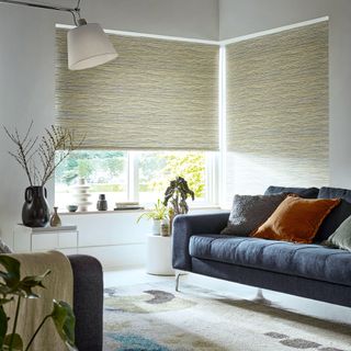 White living room with blue sofa and corner window dressed with neutral honeycomb blinds