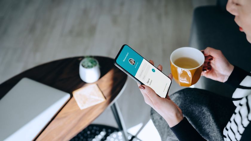 Young Asian woman relaxing at home drinking a cup of tea, logging in to her smartphone device.