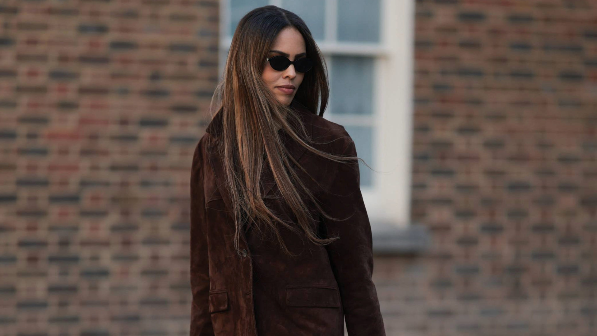 Woman styling her long hair with sunglasses and a brown jacket