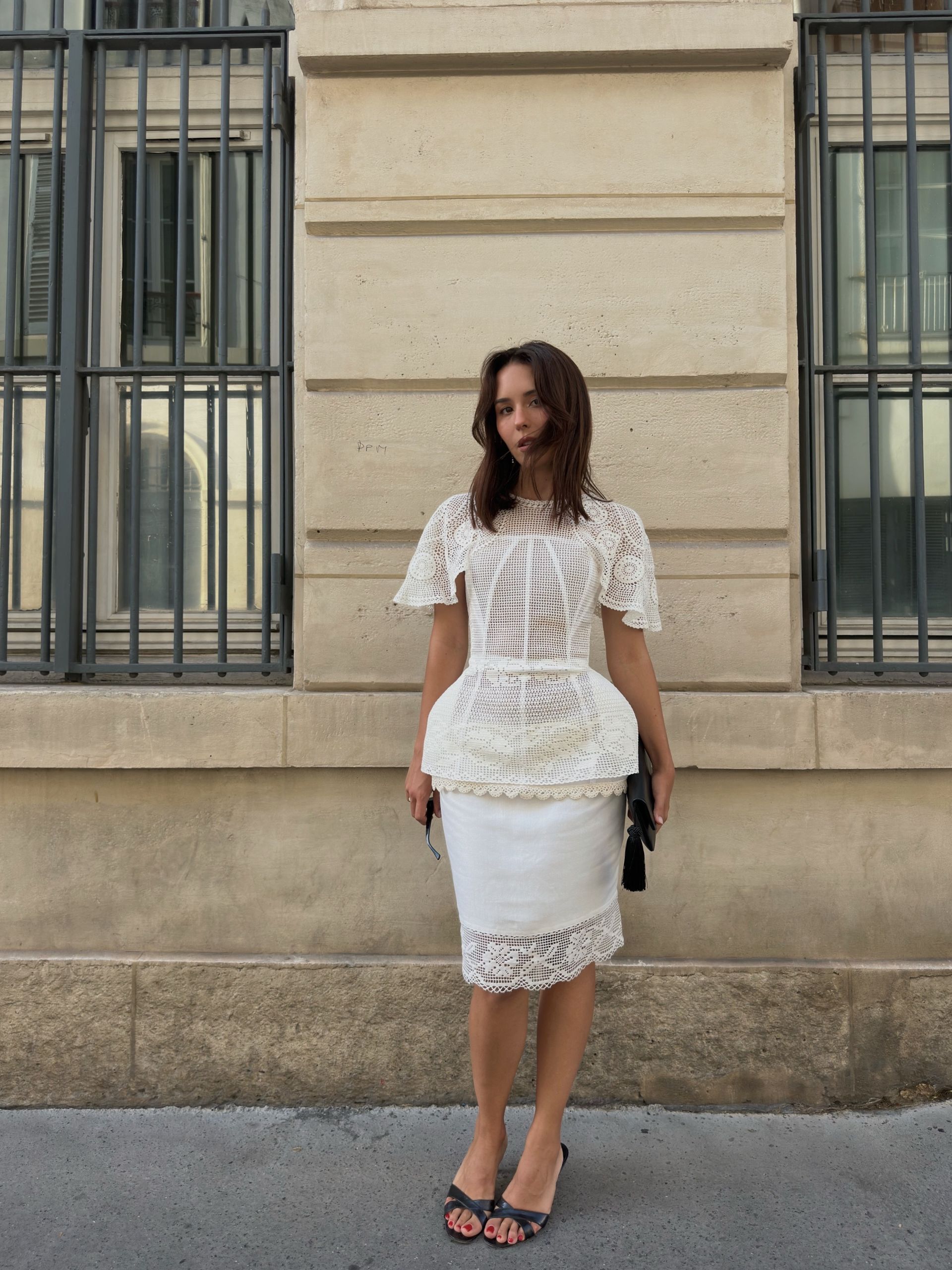 Debora wears a white cinch top with a white skirt and black heels.