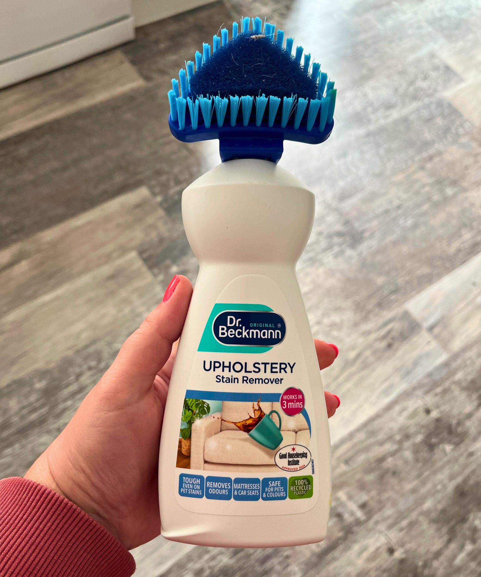 A white bottle of Dr. Beckmann&#039;s upholstery cleaner, with a blue triangular-bristle brush on the lid