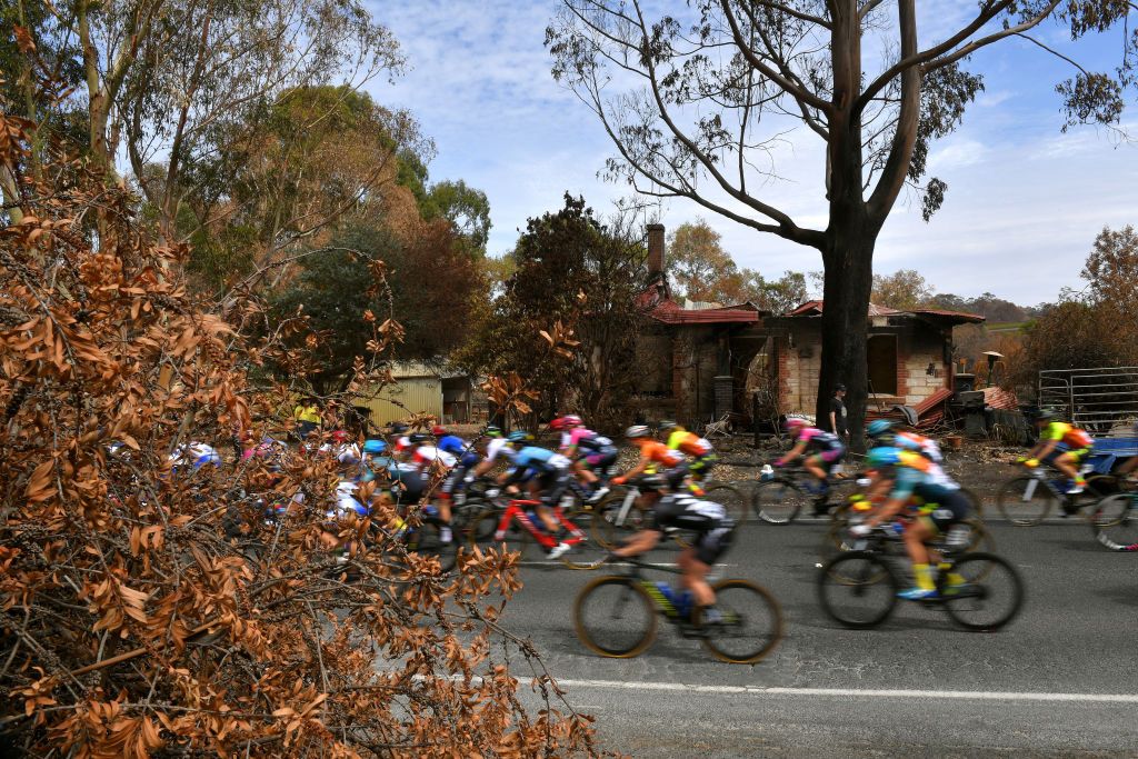 The peloton rides past a fire-hit building