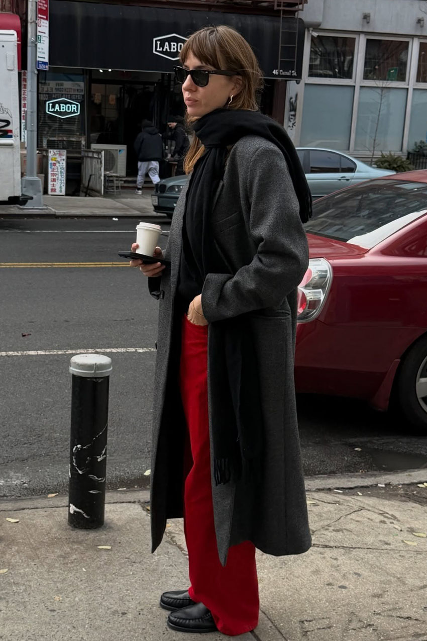 A woman wearing a gray coat, black scarf, red pants, and black loafers