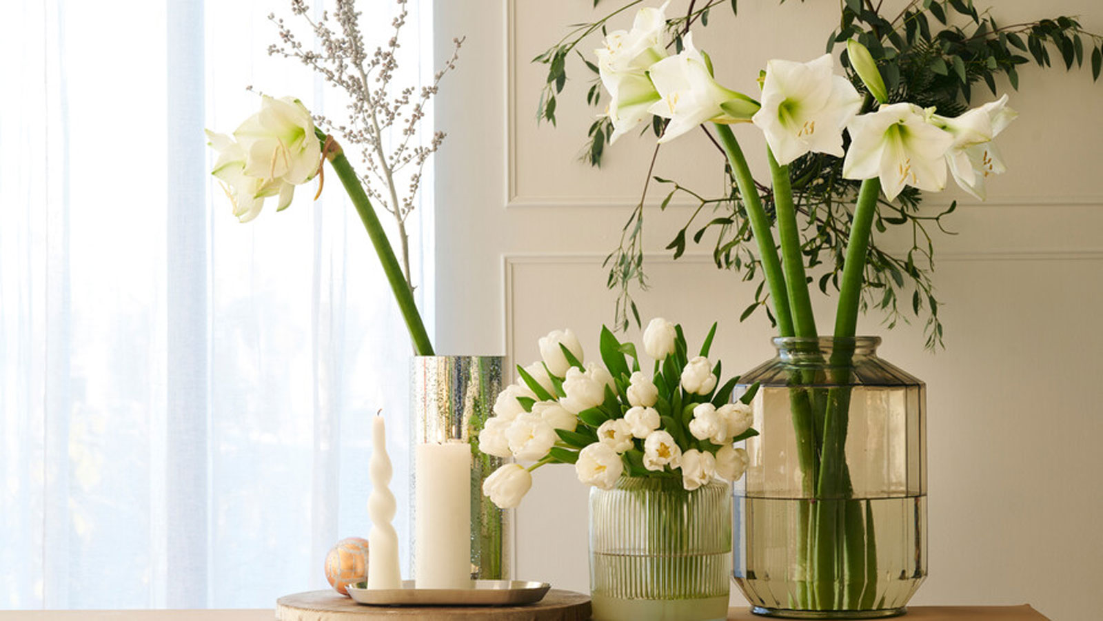 selection of white amaryllis and white tulips arranged in vases with foliage on a table