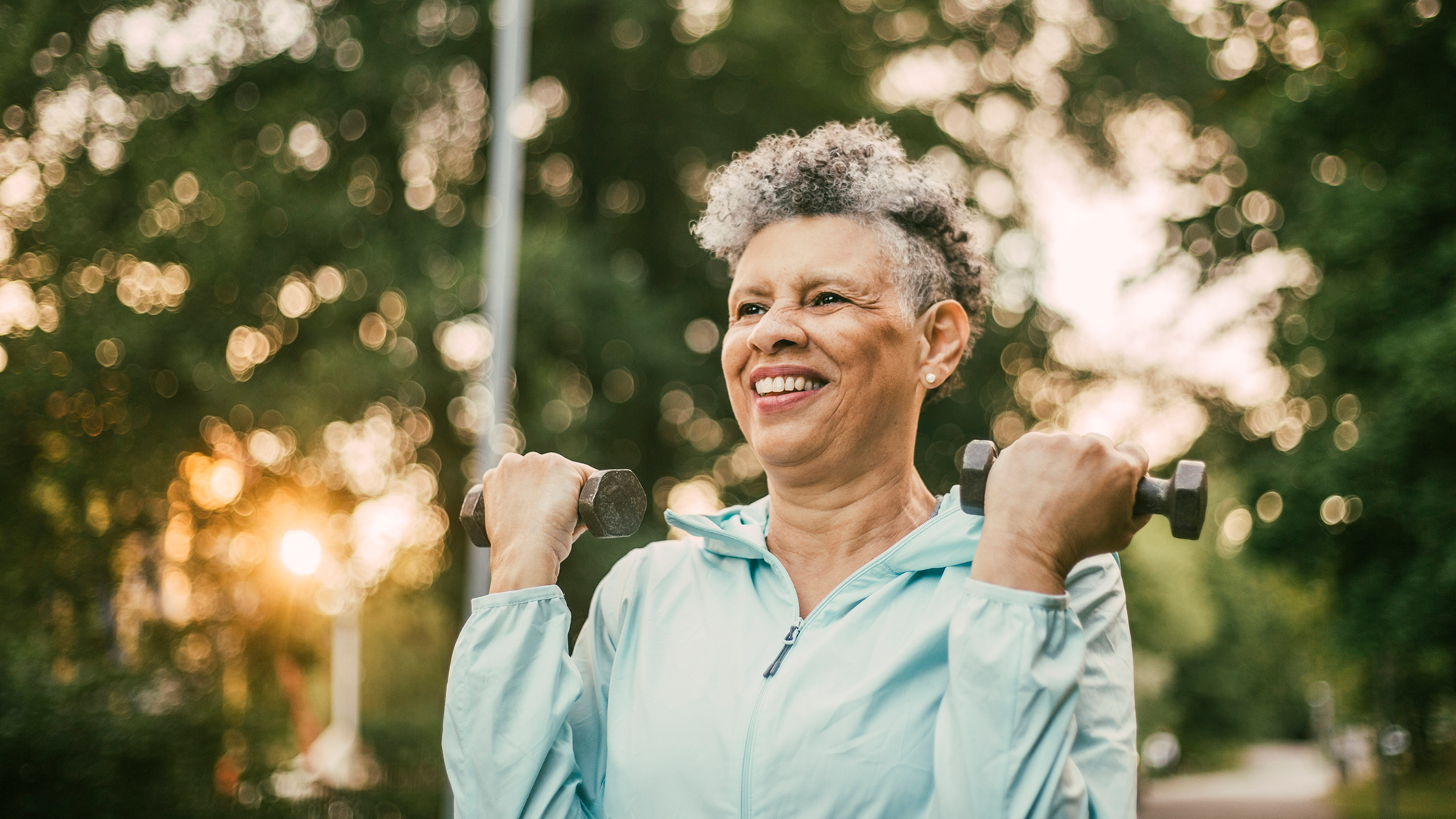 A woman with gray curly hair lifts weights using a bicep curl