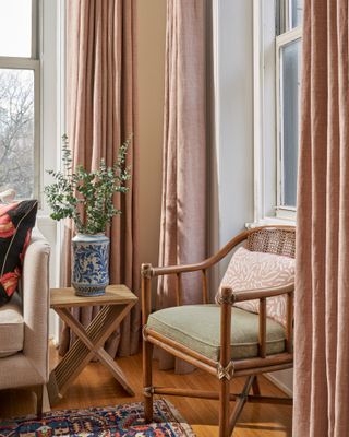 A soft pink living room with a wooden chair and long pink drapes