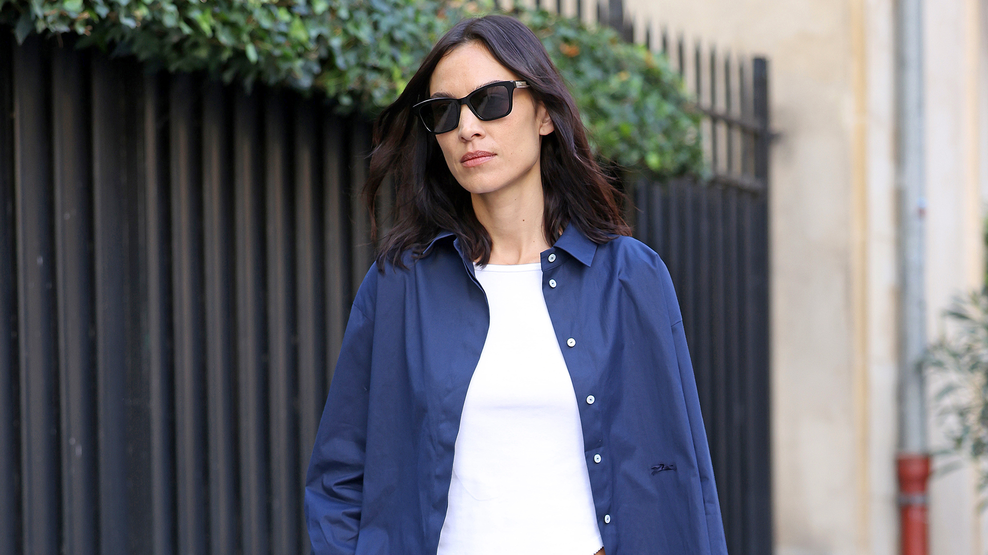 Alexa Chung wearing a blue button-down shirt over a white tee with camo pants and black ballet flats.