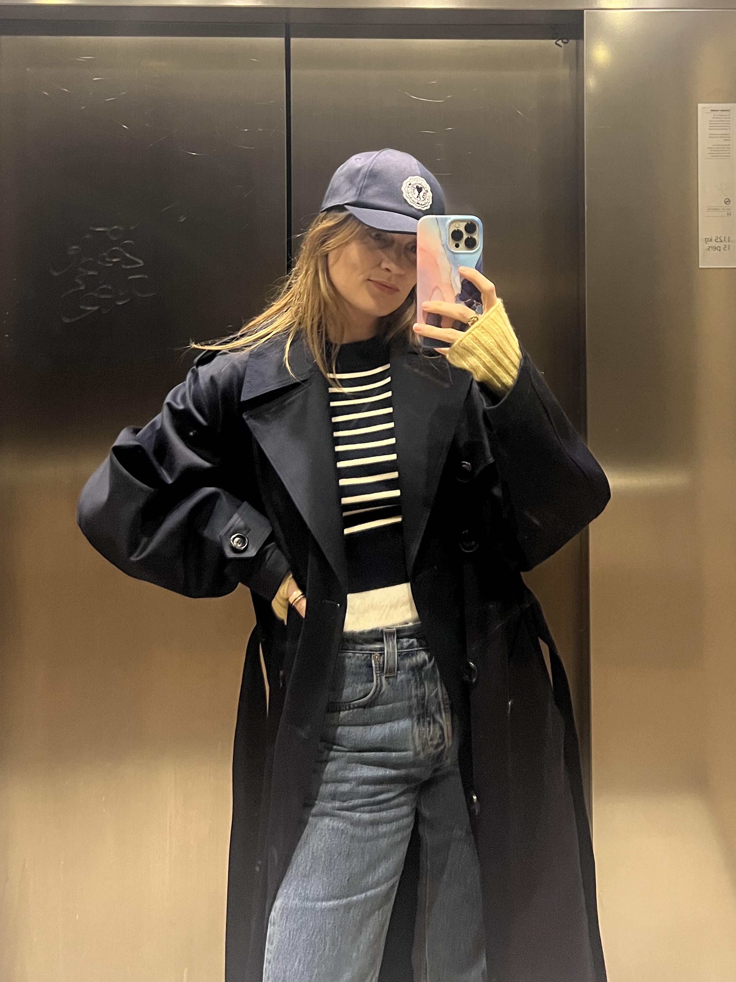 French writer and editor Eug&amp;eacute;nie Trochu poses in a baseball cap, striped sweater black trench coat, and jeans