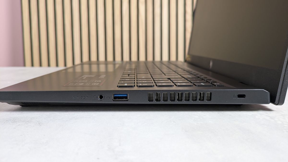 Right side ports of Acer Nitro V 15, open on desk with wooden panels and pink wall in background
