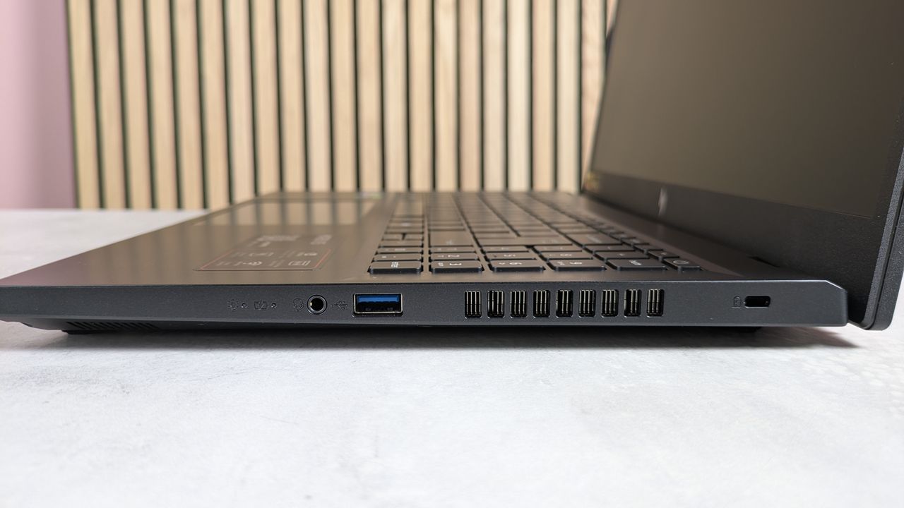 Right side ports of Acer Nitro V 15, open on desk with wooden panels and pink wall in background