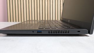 Right side ports of Acer Nitro V 15, open on desk with wooden panels and pink wall in background