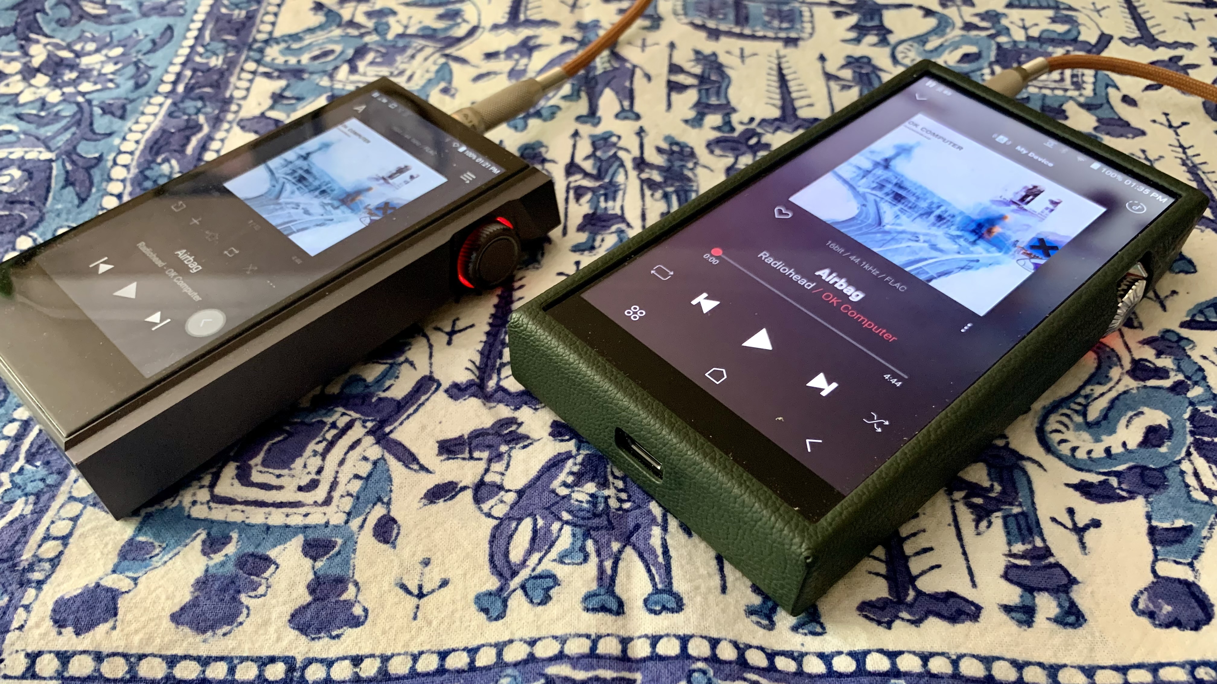 Astell & Kern A&ultima SP3000 and Astell & Kern Kann Max side by side, honing in on the volume dials, on a blue and white tablecloth