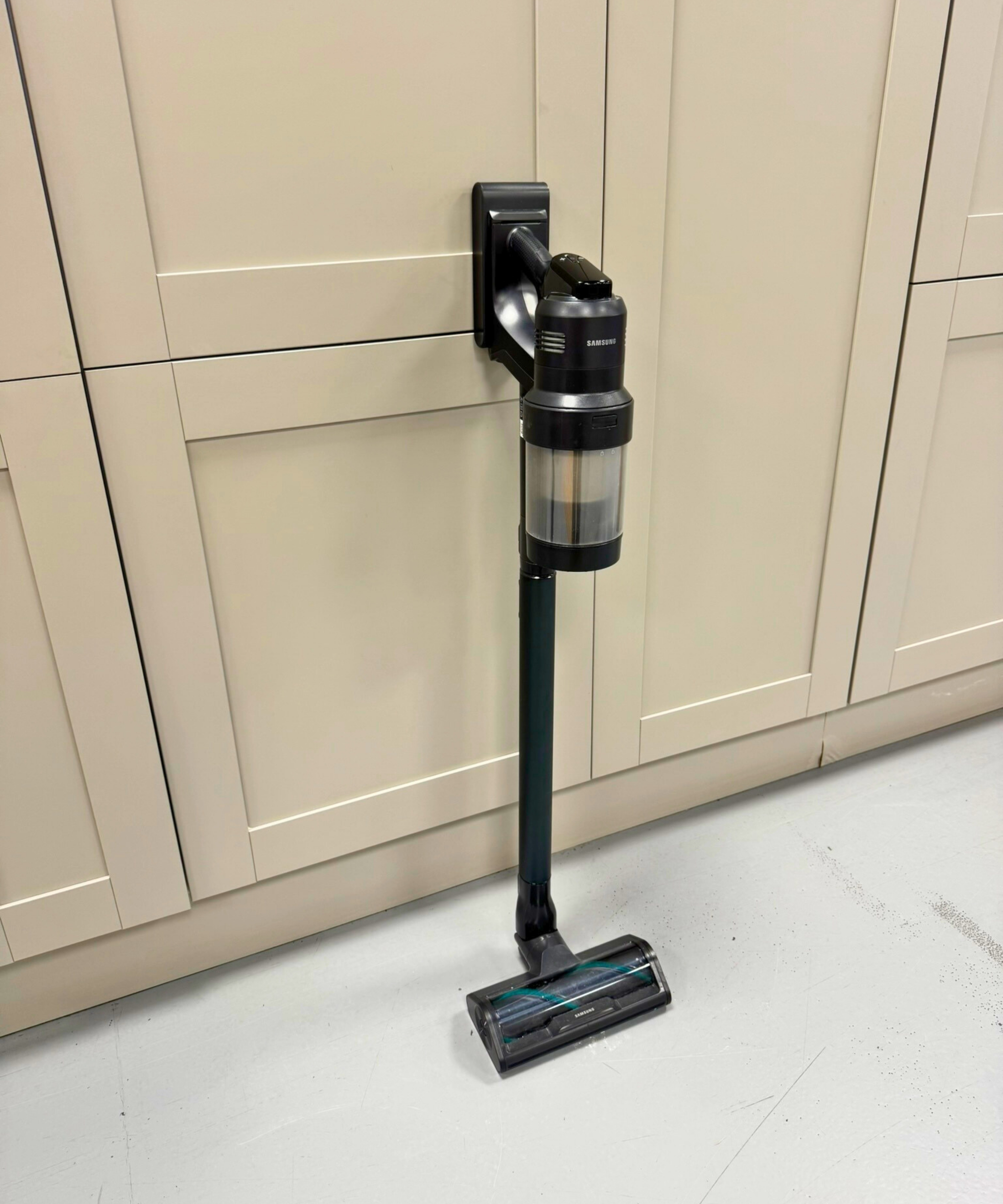 Samsung Bespoke AI Jet Ultra cordless vacuum leaning on cabinet on gray floor.