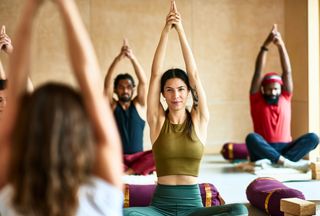 Multi-ethnic group in yoga studio sitting on floor with arms above heads