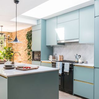 Kitchen with duck egg blue painted cabinets, marble splashback and exposed brick wall