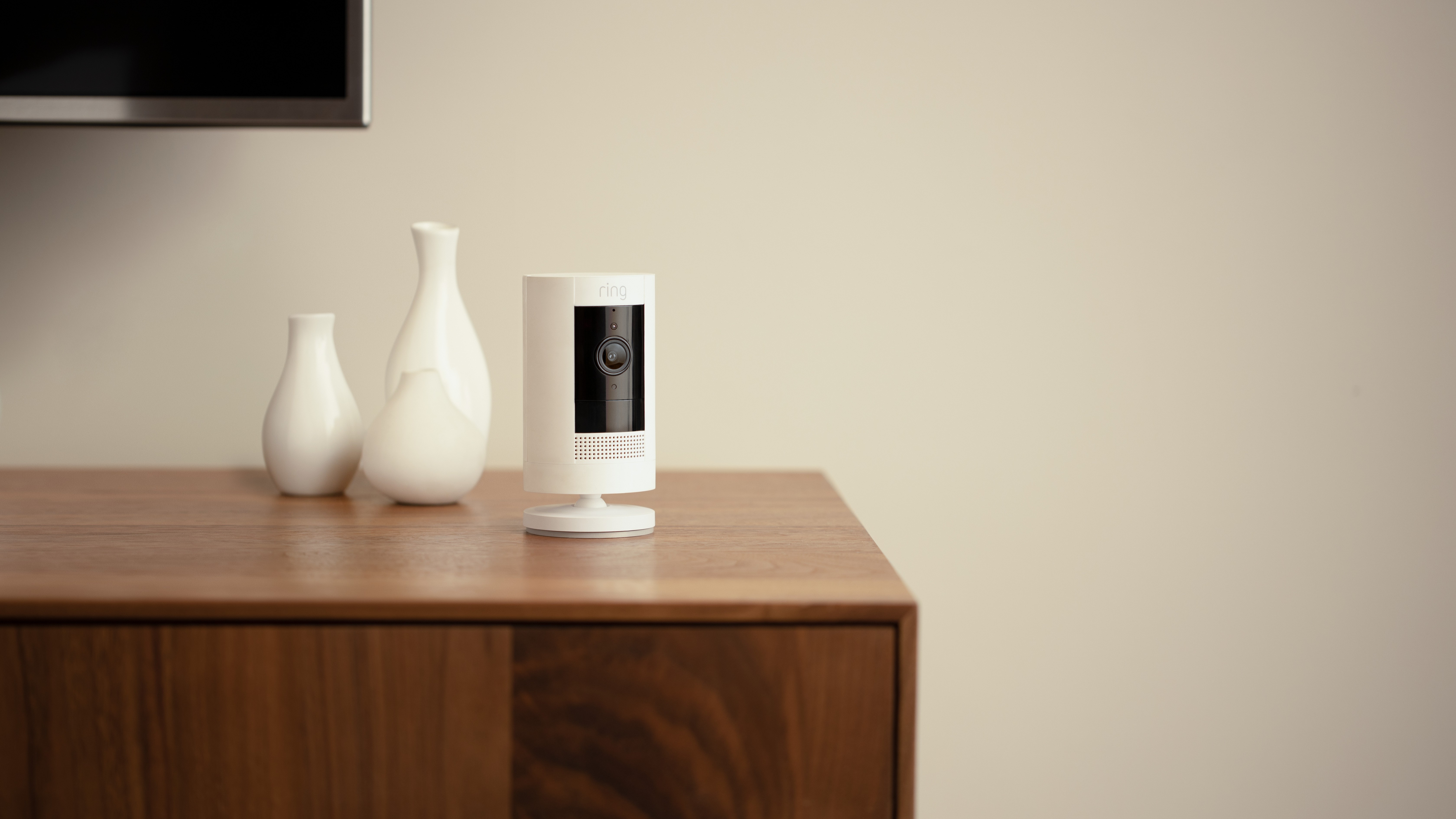 A Ring stick up cam siting on a wood table next to white vases