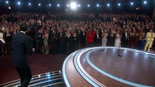 A screenshot of the crowd giving Adrien Brody a standing ovation as he walked onto the stage. In the far right hand corner, you can see Timothée Chalamet in yellow, standing and clapping. His mom is sitting next to him to his left, and Kylie Jenner is right behind him.