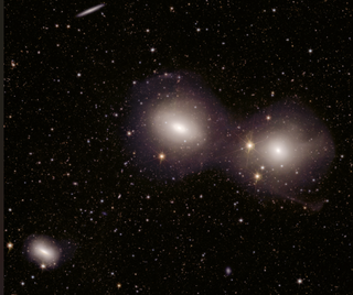A dark background of space with lots of faint and tiny spots of light. There are three hazy, white-ish blobs seen as well. Two are next to one another in the center-right and another smaller one in the bottom left.