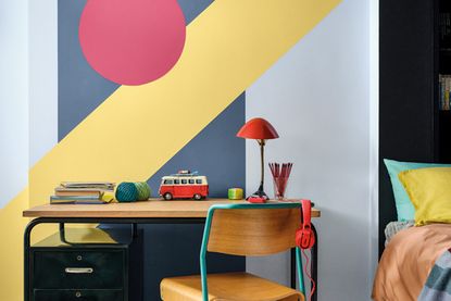 Children's bedroom with pale blue wall with dark blue, yellow and red shapes