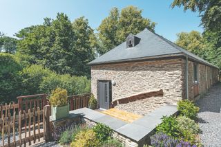 A stone barn conversion with a timber patio, a wooden fence and shrubbery