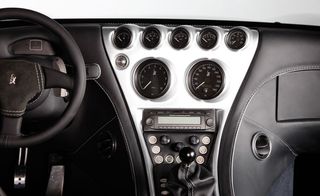 Interior dashboard view of Weissmann’s purist sports cars, black steering wheel and dials, black leather trim and silver central column