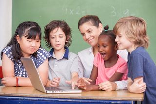 Children gather in a classroom around their teacher.