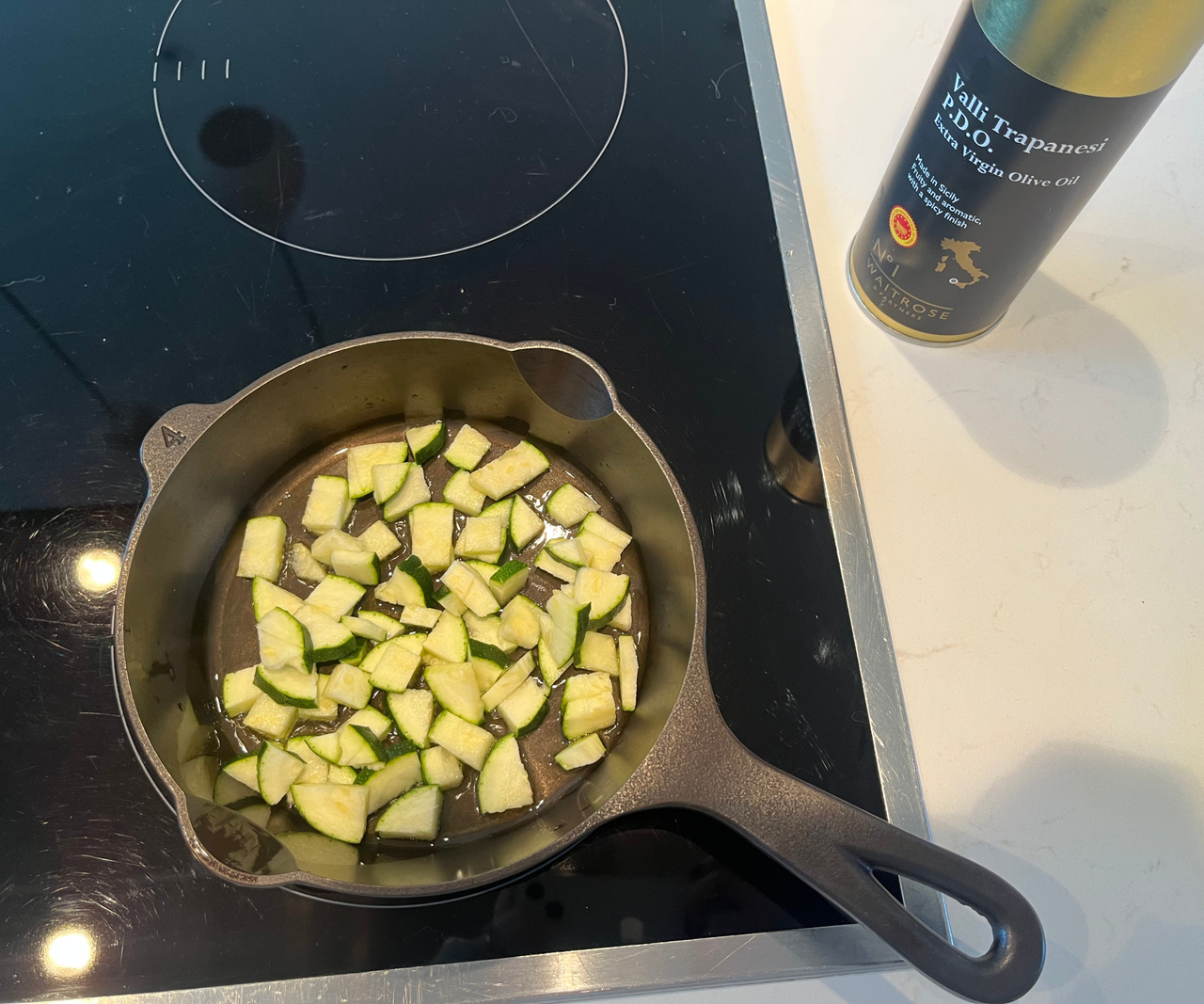 Lancaster Cast Iron Skillet on a black glass stove, filled with chopped zucchini.