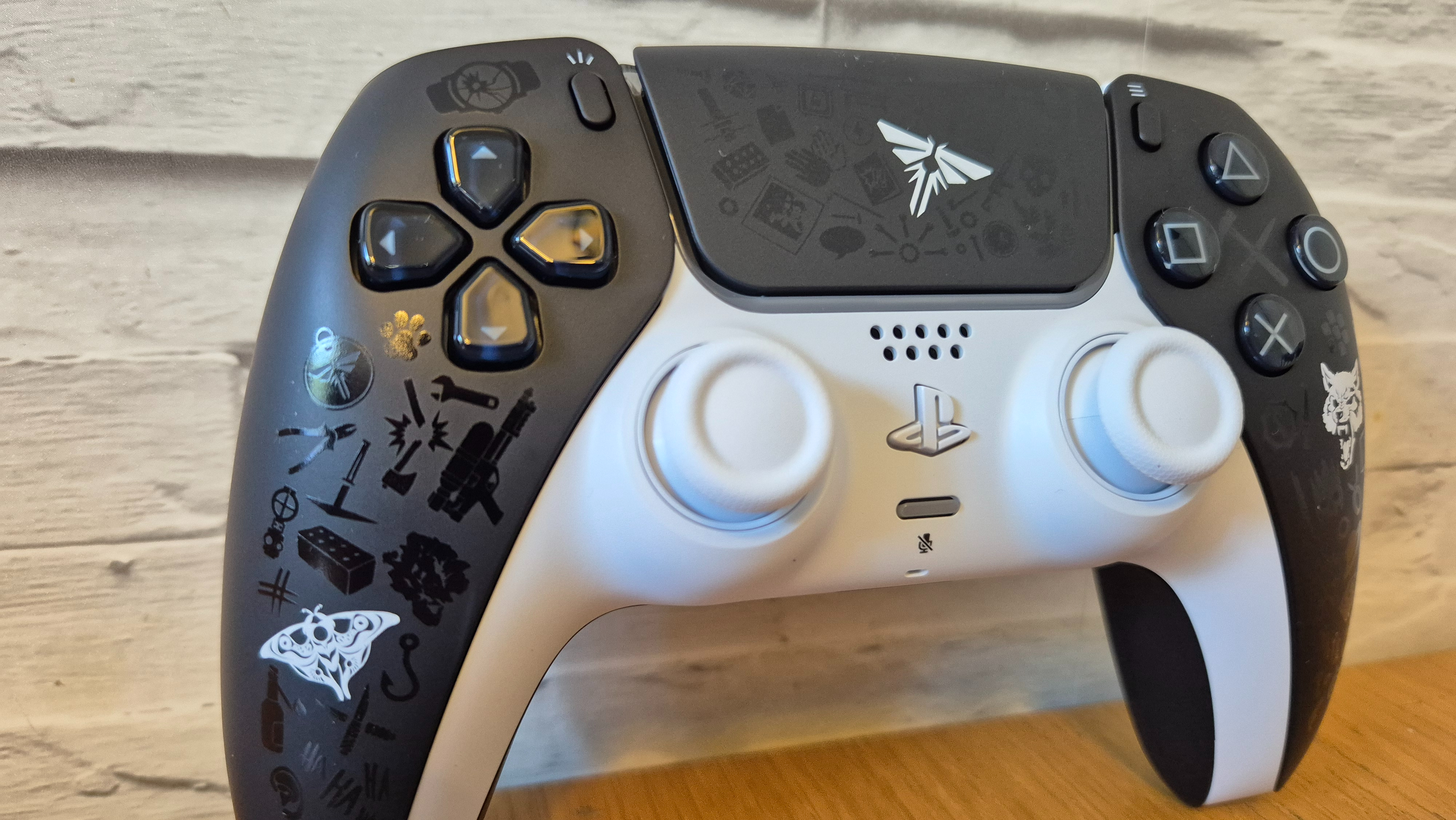 The Last of Us Limited Edition DualSense on a wooden surface in front of a white brick background